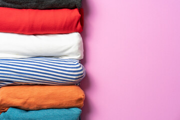 close up of rolled colorful t shirt clothes on pink table background, travel concept