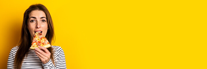 young woman bites a slice of hot fresh pizza on a yellow background. Banner