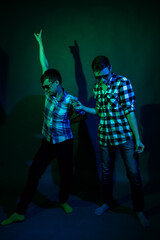 Two young men in plaid shirts dance in the studio with multicolored light