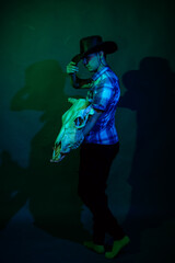 A guy in a cowboy hat and a plaid shirt in a studio with blue and green light