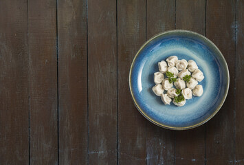 Russian pelmeni meat Dumplings with greens in a blue plate on wooden background. Copy space, top view.
