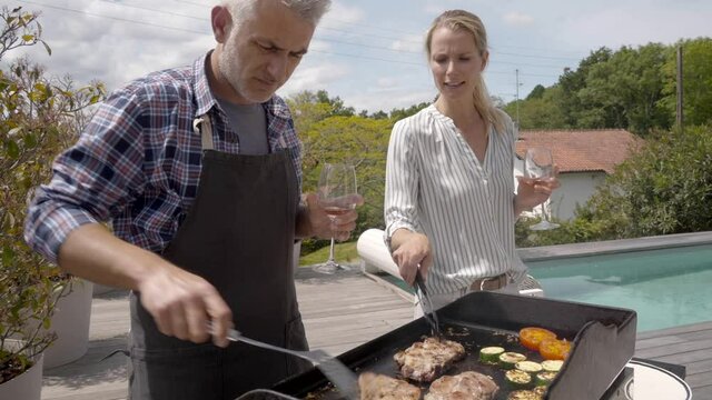 Cheerful couple cooking meat and vegetables on grill 