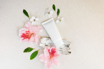 white cosmetic tube with fragments of bark and flowers on a light background. Perfumed cream concept