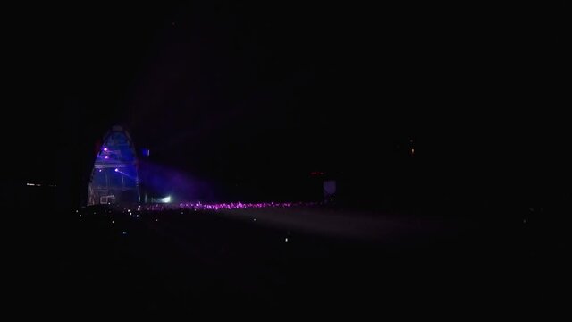 Strobe lights from the stage illuminate the crowd of fans. People jump up and put their hands up. Live concert of a popular band. Happy music lovers have fun at the fest.