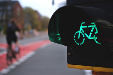 close up on bicycle traffic light in yellow housing showing green light at an urban intersection with moving cyclist in background - selective focus with excessive blur