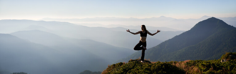 Sporty beautiful young woman doing meditation on one leg on fresh air in incredible mountains. Panorama. Concept of harmony with freedom and nature.