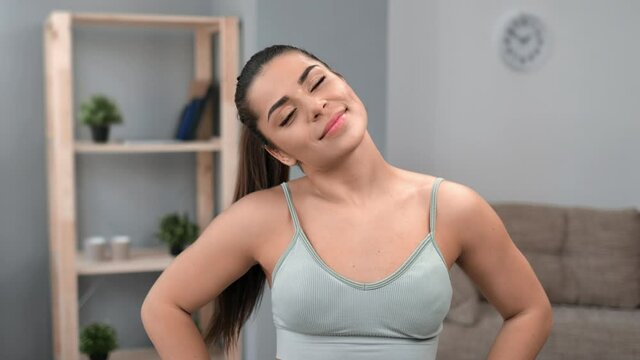 Portrait of smiling young brunette fitness woman performing neck warming up training at living room