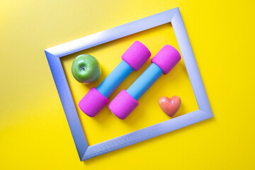 in a metal frame are pink dumbbells, a green apple and a heart
