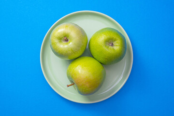 green plate with green apples stands in the center of the blue background
