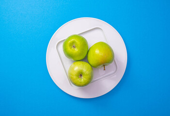a white plate with green apples stands in the center of a blue background