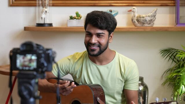 Young Asian man is playing the guitar on social media by streaming live from his home.Young musician blogger is recording video for internet music blog playing guitar and talking using camera indoor.