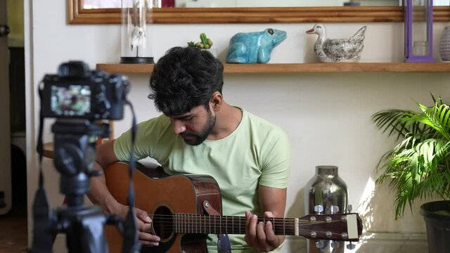 Asian man filming video himself playing guitar in the room at home using camera for recording guitar performance. professional guitarist casting to online audience.work from home concept.