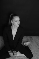 black and white photo of a Russian girl, in a black jacket on a naked body, black jeans, sitting on the floor, look to the side, beautiful profile, blonde long hair, ponytail hairstyle