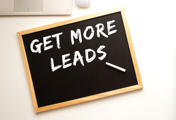 Text GET MORE LEADS written in chalk on a slate board. Office desk.