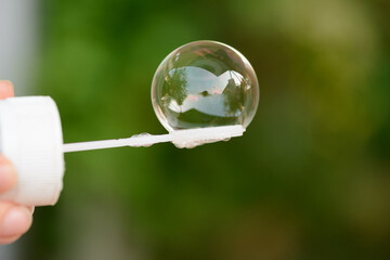 The hand holds a stick with a soap bubble on a green background