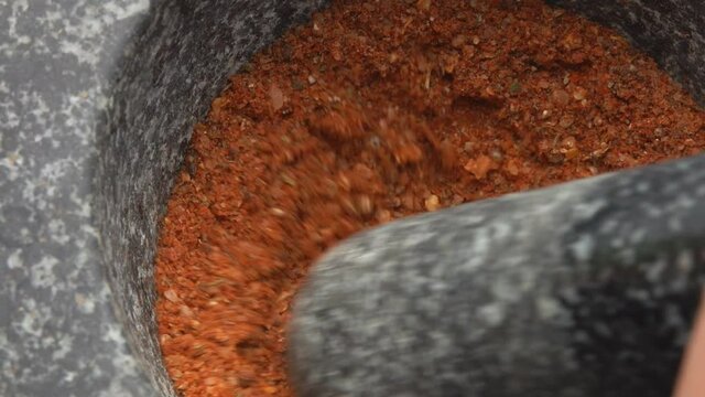 Heavy pestle is grinding and mixing spices, peppers and sea salt in the mortar