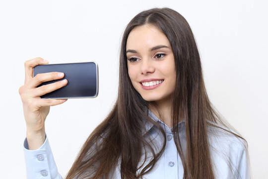 Portrait of brunette young woman smiling and taking selfie photo with smartphone isolated on white background