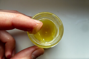 Gelbe Salbe in einem runden Glas wird von einem Finger prüfend entnommen. Zähflüssige gelbe...