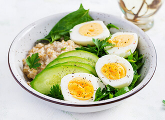 Breakfast oatmeal porridge with boiled eggs, cucumber and green herbs. Healthy balanced food.