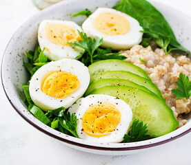 Breakfast oatmeal porridge with boiled eggs, cucumber and green herbs. Healthy balanced food.