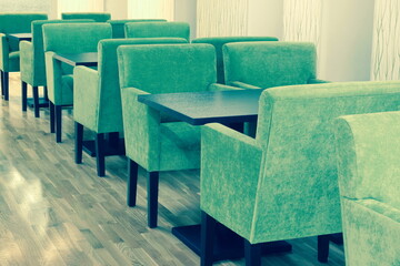 Modern Cafe Or Restaurant Interior With Comfortable Furniture. Empty Soft Green Armchairs And Brown Wooden Tables In Row At The White Wall On The Laminated Floor.