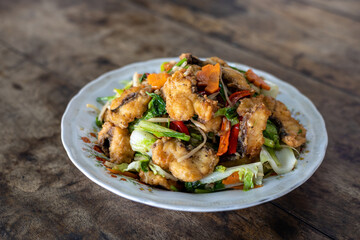 Stir-fried fish and vegetables in a plate placed on a wooden table.
