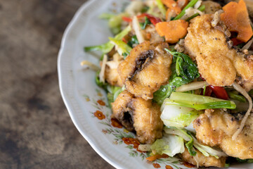 Stir-fried fish and vegetables in a plate placed on a wooden table.