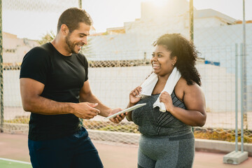 Trainer working with curvy african woman while giving her instruction with digital tablet during training session - Sport people lifestyle concept