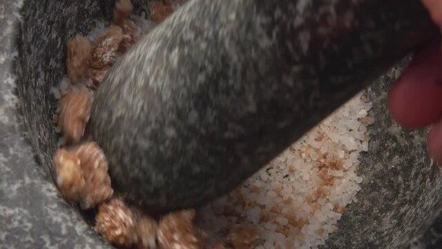 Close-up of the pestle grinding salt and brown sugar in the stone mortar