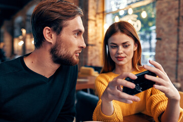 a woman in a sweater with a mobile phone and a guy with a beard are sitting in a restaurant