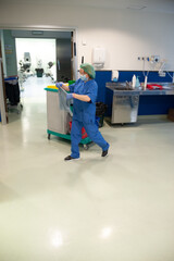 Woman from the cleaning service of a hospital walking while spreading the cloth to clean in the previous operating room. sanitary concept