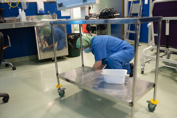 Woman from the cleaning service of a hospital crouching cleaning a portable operating table in the previous operating room. Sanitary concept