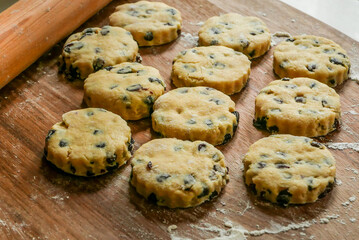Preparing scones for baking on a floured wooden board with rolling pin