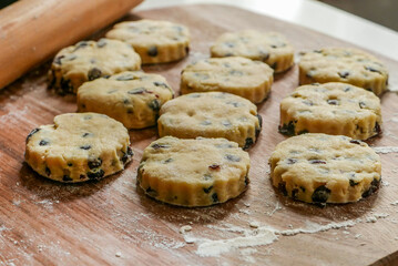 Preparing scones for baking on a floured wooden board with rolling pin