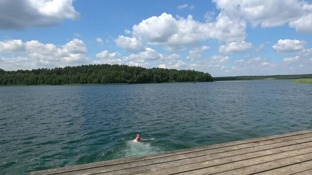 Mann springt von einem Holzsteg in den See