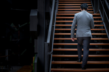 Back view of businessman walking up staircase, modern building. Copy space.