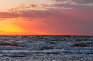 Stunning sunset reflections on the crashing sea waves. Red and orange background and light clouds.