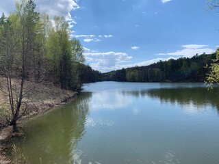 calm lake surface in beautiful forest surroundings. 
Spring landscape with trees around a lake against a blue sky.