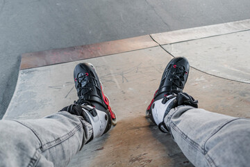  man legs in roller skates sits on a ramp in skatepark.in the background the stadium and...