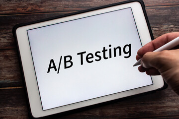 Tablet displaying “A/B Testing” on white background. Man hand holding wireless stylus pen in image. A/B testing is a user experience research methodology