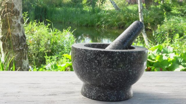 The hand is putting a mix of spices, peppers and salt into the grey stone mortar