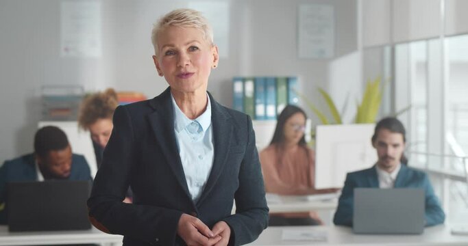 Mature businesswoman looking at camera and talking standing in co-working office