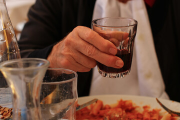 Close-up of hand raising glass with red wine for a toast, photo taken at outdoor restaurant in front of a plate of pasta.
