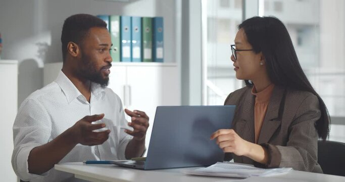 Diverse business colleagues looking at laptop and discussing project in office