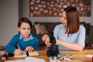 Aunt and nephew do homework together. Women explain kid writes in notebook. Schoolboy studying at home. Family relationships, primary education, childhood