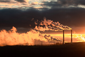 Fototapeta premium the smoke from the chimneys of the plant during sunset is illuminated by the sun from the back