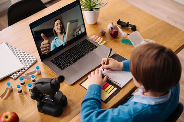 A Preteen boy uses a laptop to make a video call with his teacher. The Screen shows an online...