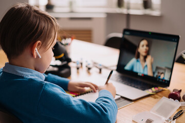 A Preteen boy uses a laptop to make a video call with his teacher. The Screen shows an online...