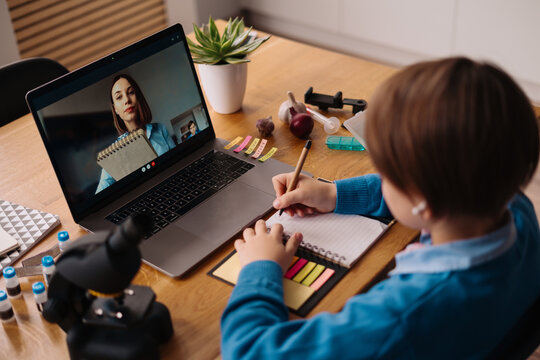A Preteen boy uses a laptop to make a video call with his teacher. The Screen shows an online lecture with a teacher explaining the subject from class.