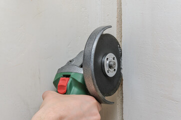 Construction worker sawing a hole in the wall for electrical wiring with a grinder	
